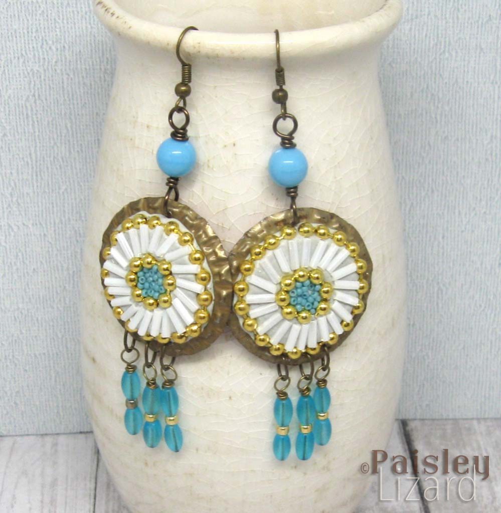 Bead and epoxy clay mosaic earrings hanging on a bottle.