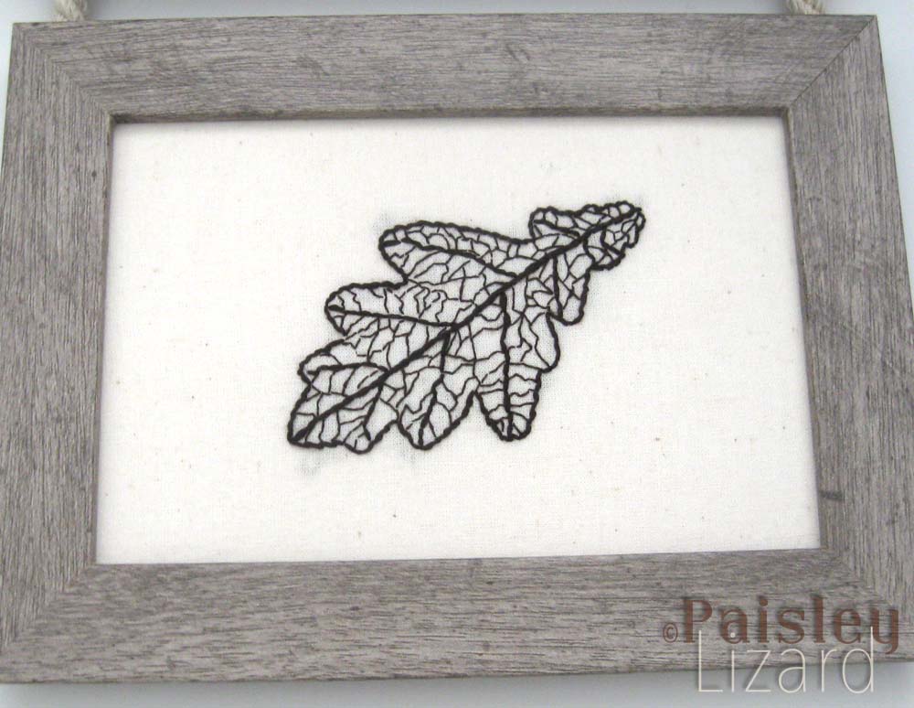 Embroidered oak leaf skeleton in distressed wood frame.