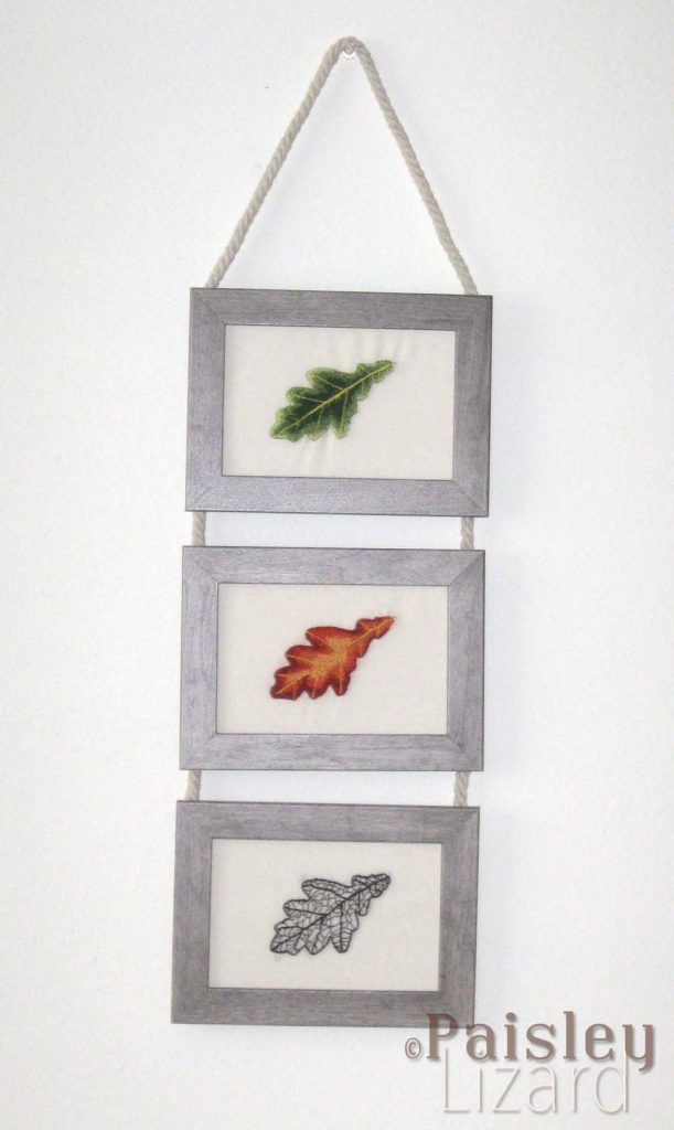 Wall hanging with green, red, and brown embroidered oak leaves in wood frames