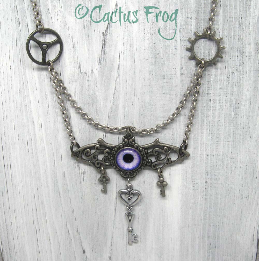 Antiqued silver flying eyeball necklace hanging on whitewash wood backdrop.