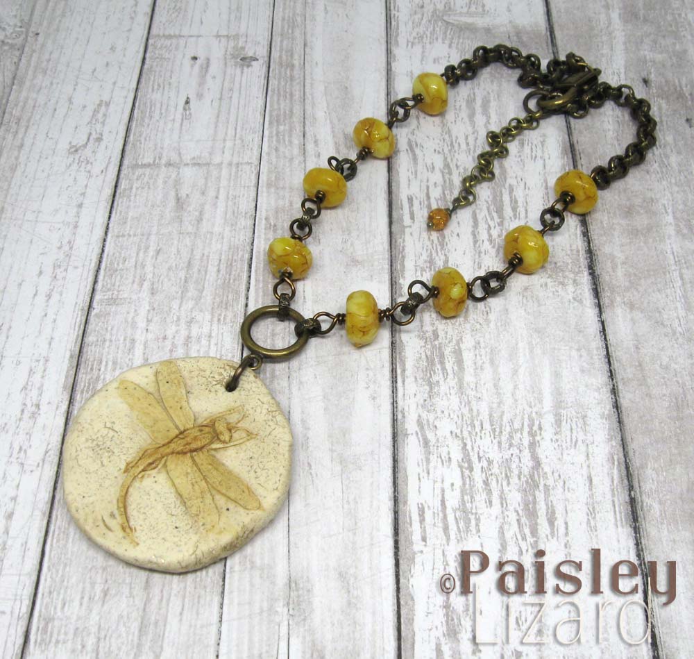 Necklace with faux dragonfly fossil pendant on faux amber beaded chain.