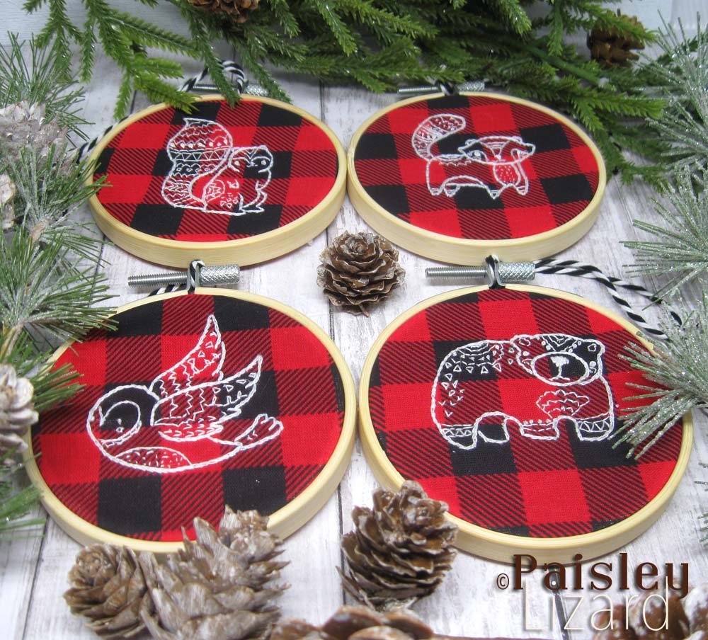 Set of four embroidered ornaments surrounded by winter greenery