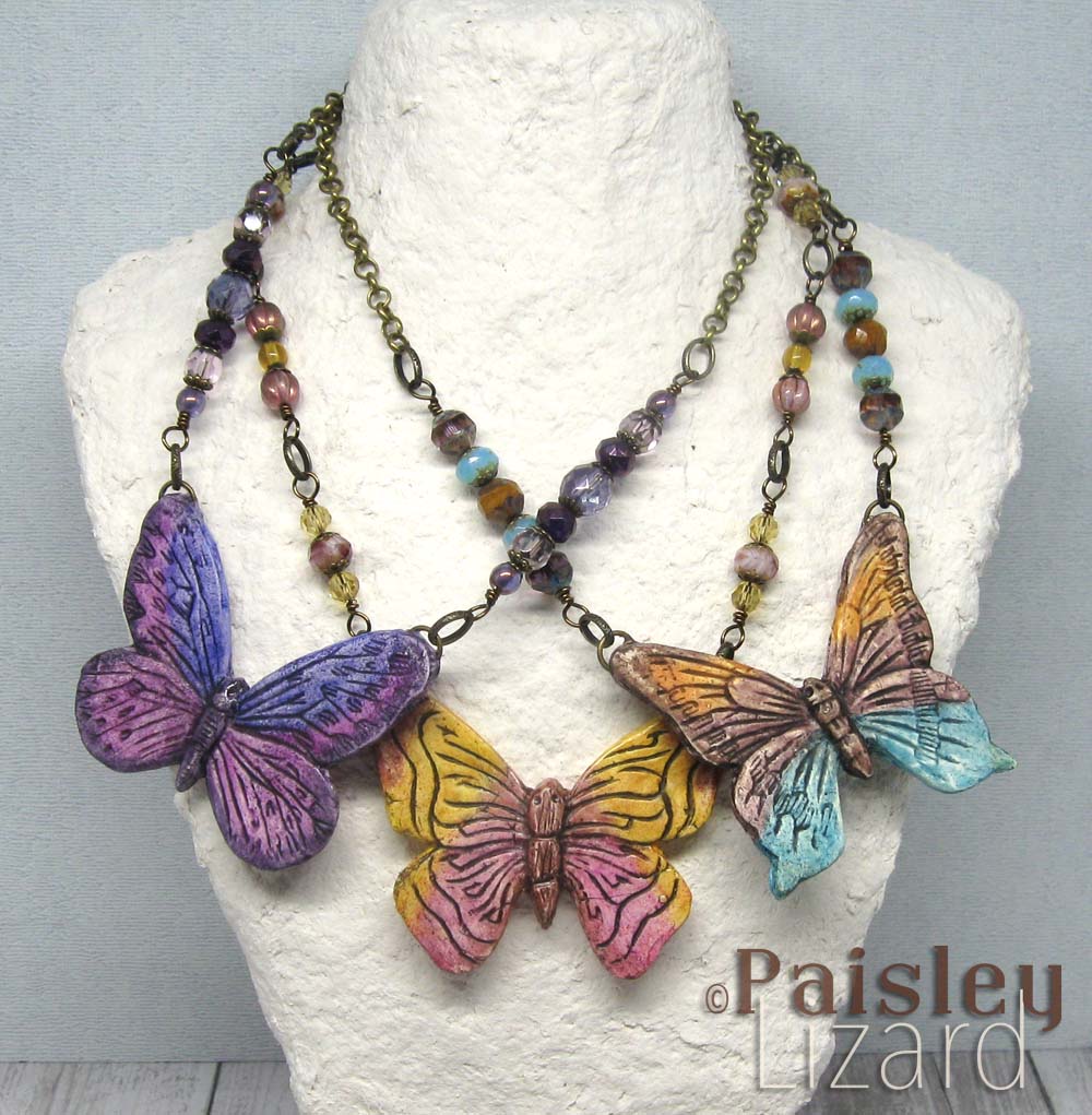 Three painted butterfly necklaces on display bust.