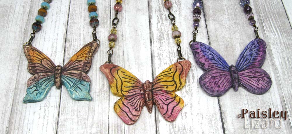 Three painted butterfly pendant necklaces flat on wood