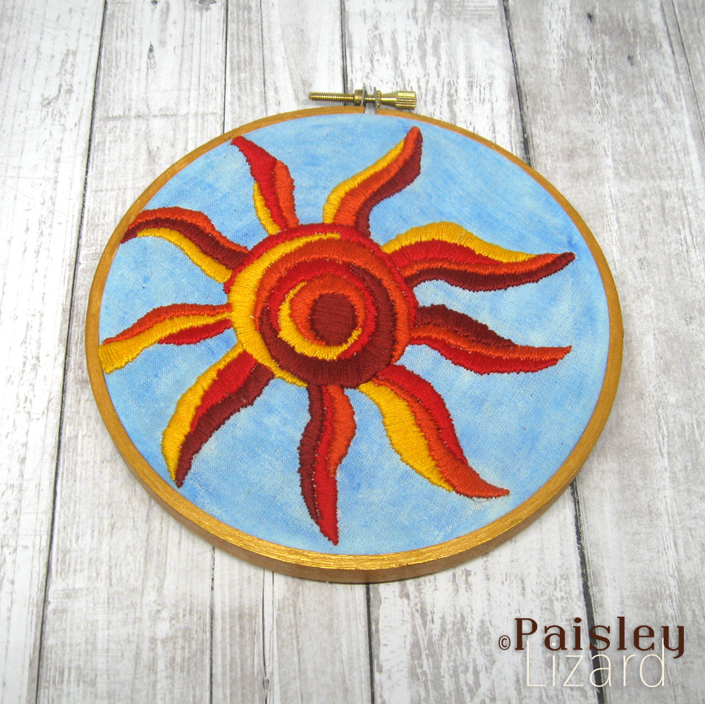 Solstice sun embroidery in wood hoop.