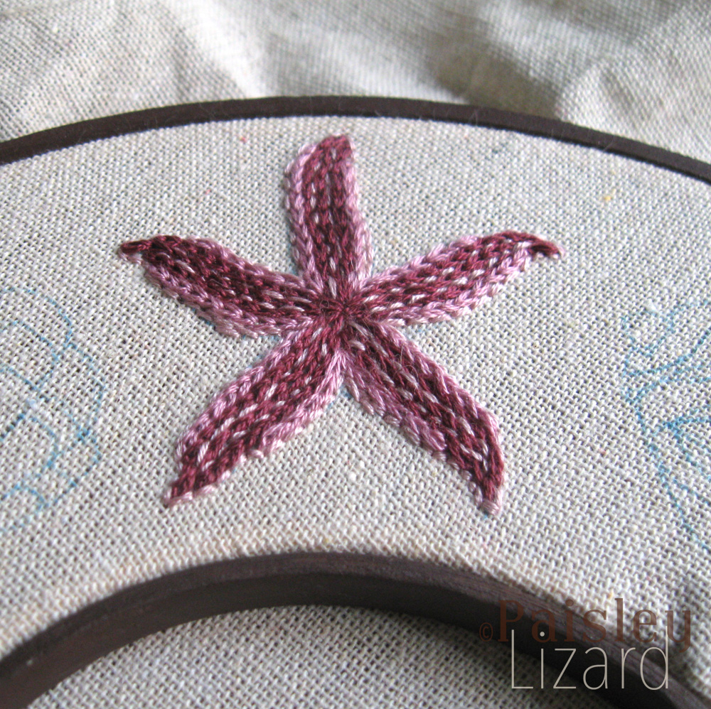 Violet and pink starfish embroidered on beige linen fabric.