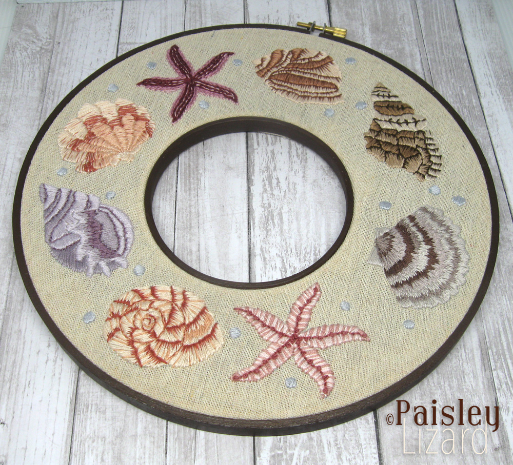Double-hoop embroidered wreath with seashells on linen fabric.