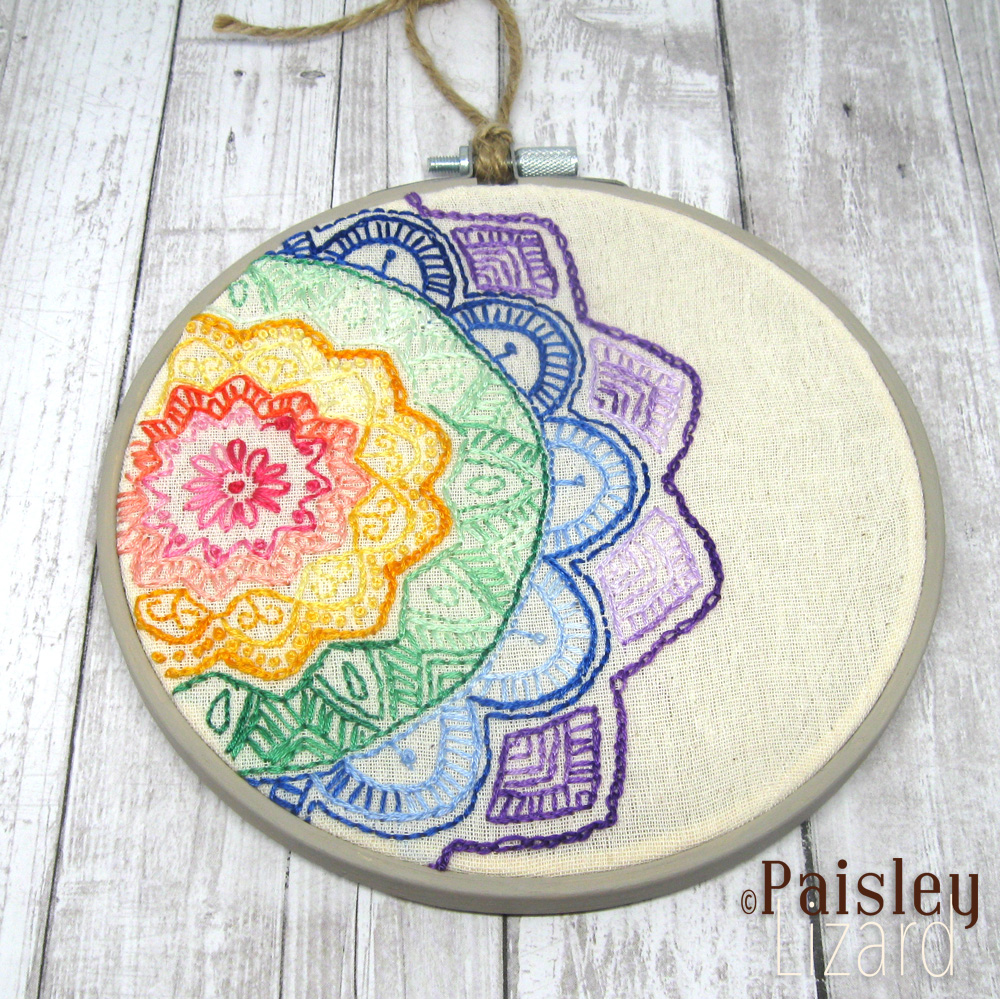 Rainbow mandala pattern embroidered on cotton fabric in wood hoop.