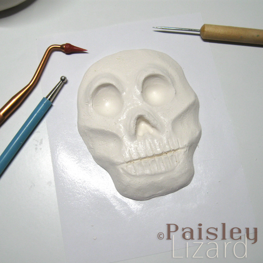 Raw polymer clay skull sculpture in relief on work table