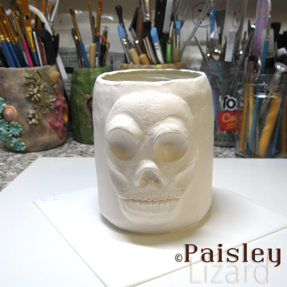 Raw clay over glass jar with skull sculpture on work bench