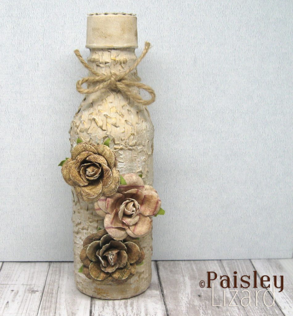 Shabby chic altered bottle with gilded ivory base and three paper flowers.